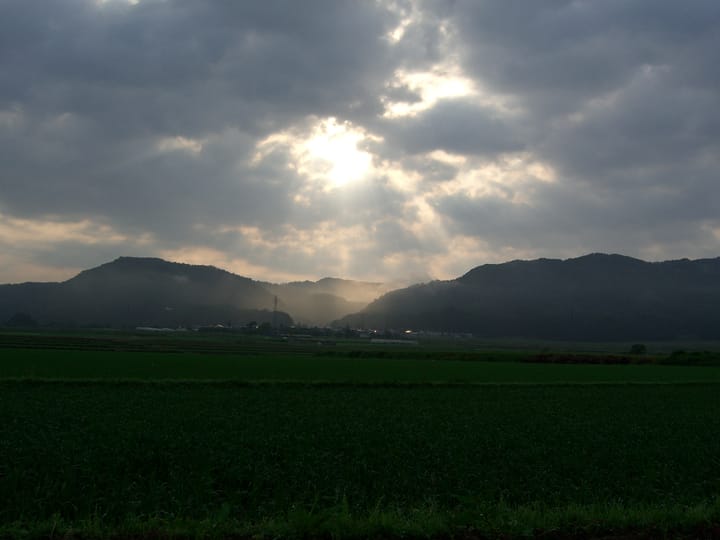 A few of rice fields in Nishiaizu, Fukushima, with hills in the background and the morning sun shining through the clouds.